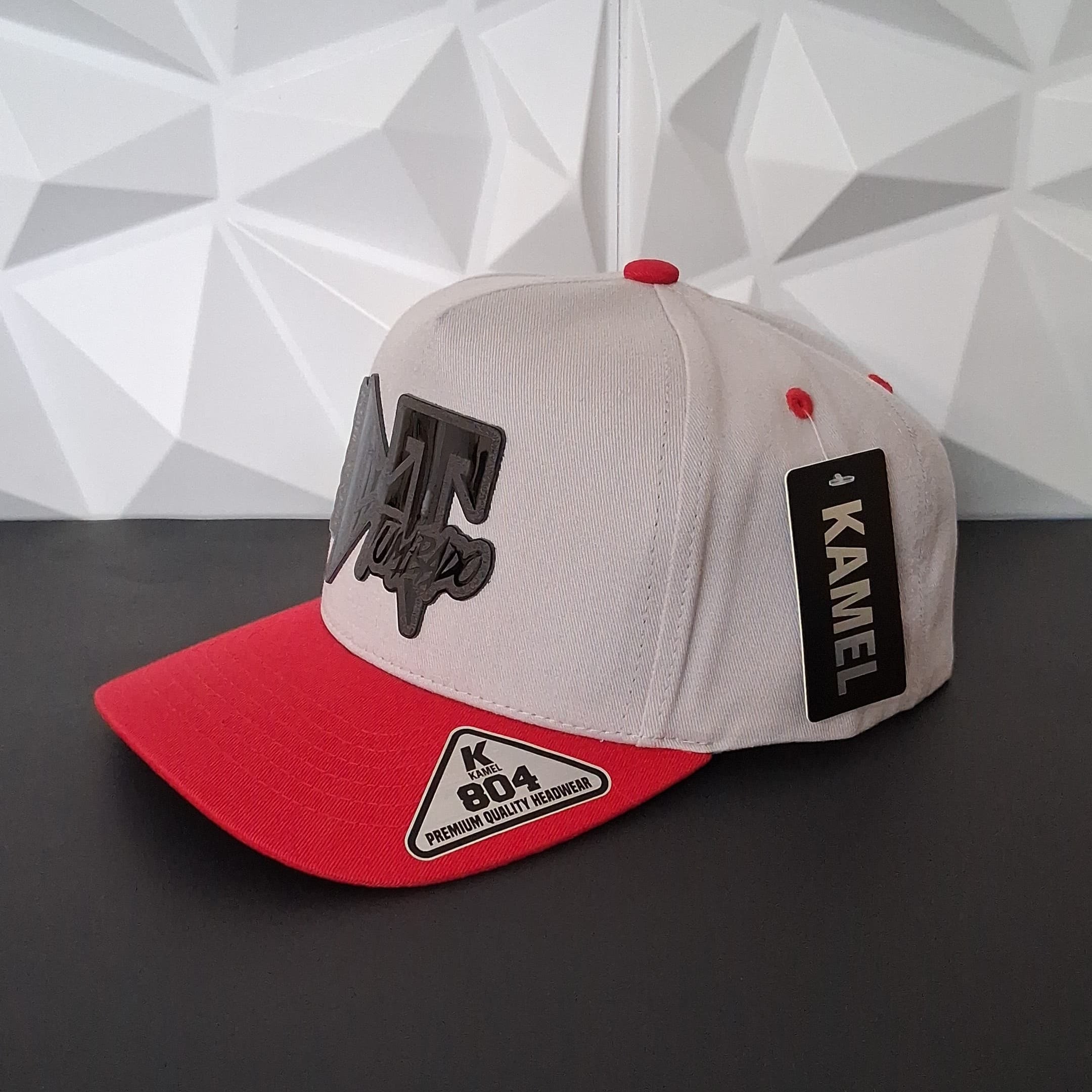 Baseball cap with red brim and white front against a geometric-patterned wall.